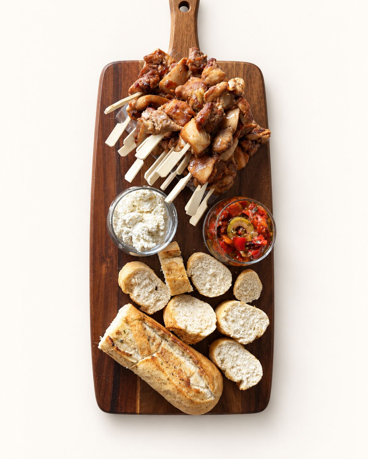 Houten plank met kipspiesen, brood en twee dips.