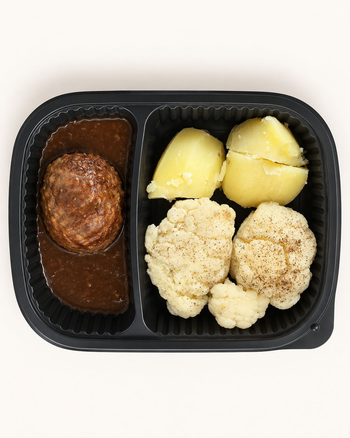 Maaltijdbak met bloemkool, gekookte aardappelen en een gehaktbal in jus.